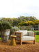 Andalusian Platform Grand End Table beside a timber-framed armchair on a gravel garden terrace
