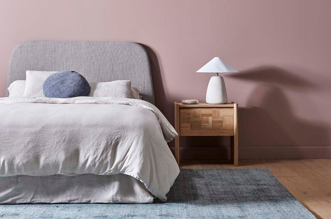 Tepih Dune Rug in Sacramento, beside a bed with grey linen and a timber bedside table