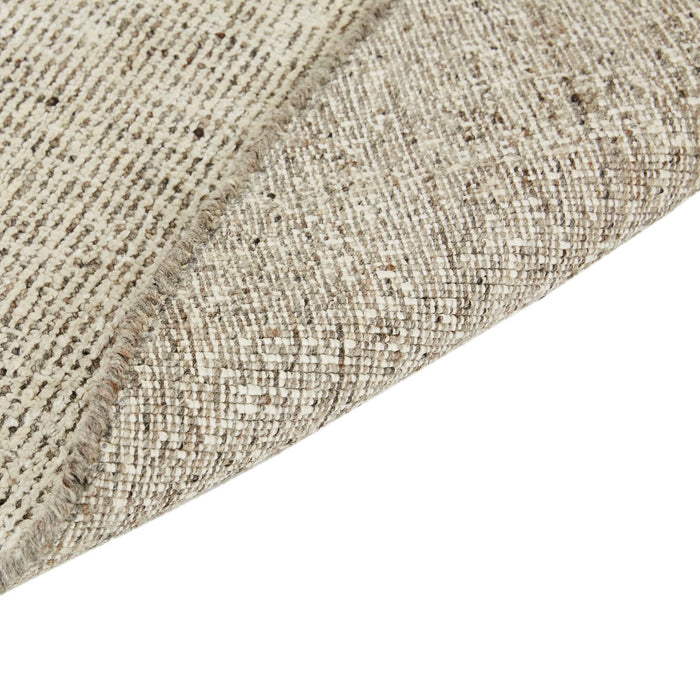Tepih Dune Round Rug in Oatmeal, close-up of the curved edge folded over, showing the flecked weave