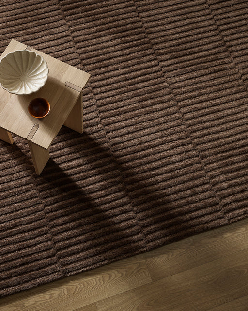 Anni Floor Rug in Chocolate, seen from above with a pale timber side table, showing the ribbed texture