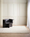 Anni Floor Rug in Oat, in a panelled room with a dark sculptural armchair on herringbone floors