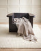 Anni Floor Rug in Oat, under a dark sculptural armchair with a draped striped throw