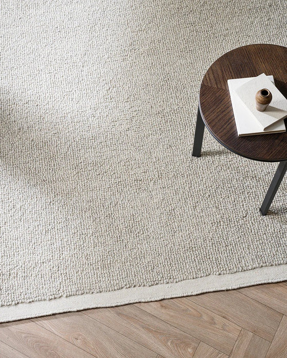 Clifton Floor Rug in Bone, seen from above beside a dark timber stool with books