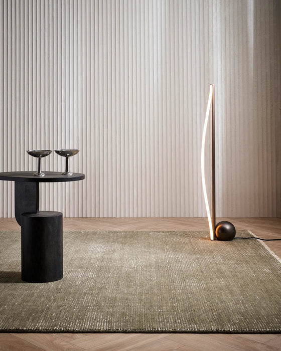 Corbett Floor Rug in Lichen, in a room with a dark side table and a curved floor lamp
