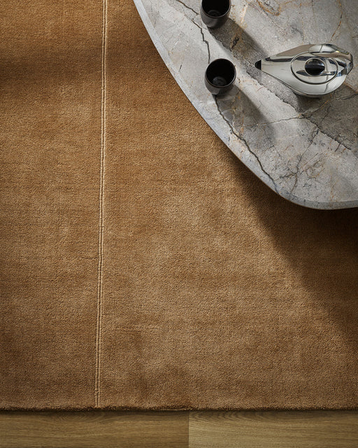 Bastion Floor Rug in Hazelnut, seen from above beside a marble coffee table, showing the pile and seam detail