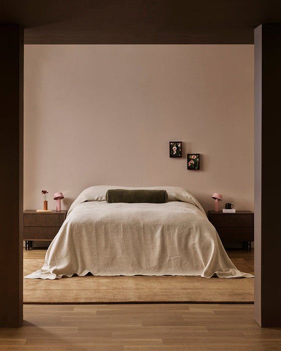 Bastion Floor Rug in Hazelnut, under a bed with cream linen and a green bolster in a bedroom