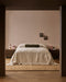 Bastion Floor Rug in Hazelnut, under a bed with cream linen and a green bolster in a bedroom