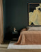 Beckett Floor Rug in Straw, beside a bed with terracotta linen in a bedroom with dark green walls