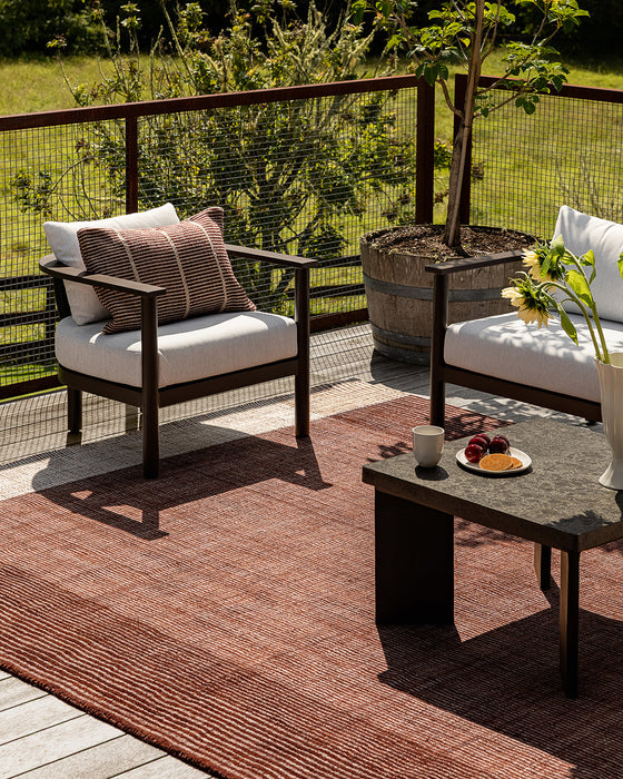Bedrock Floor Rug in Claret, on an outdoor timber deck with dark armchairs and a stone coffee table