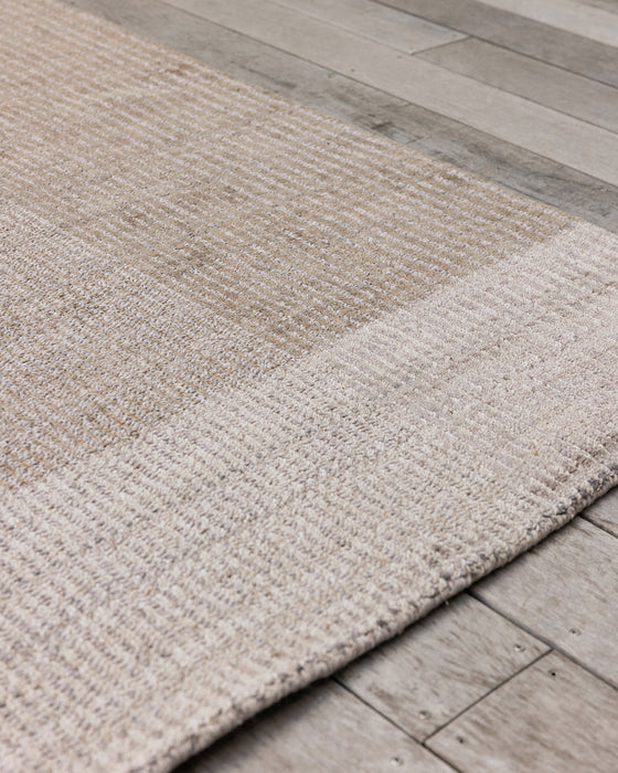Bedrock Floor Rug in Sand, close up of a corner on timber decking, showing the woven texture