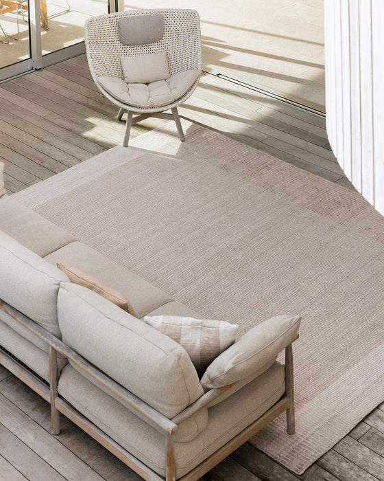 Bedrock Floor Rug in Sand, seen from above on a deck with an outdoor sofa and woven lounge chair