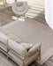 Bedrock Floor Rug in Sand, seen from above on a deck with an outdoor sofa and woven lounge chair