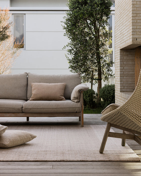 Bedrock Floor Rug in Sand, on a courtyard deck with an outdoor sofa and woven lounge chair