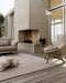 Bedrock Floor Rug in Sand, on a covered deck beside an outdoor brick fireplace and woven lounge chair