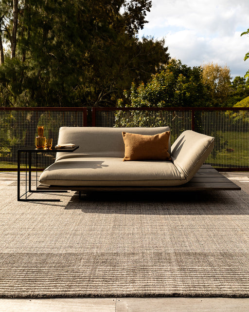 Bedrock Floor Rug in Zinc, on a timber deck with an outdoor daybed and black side table