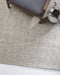 Kansas Floor Rug in Oyster/Natural, close view under a grey cushioned armchair, showing the chunky weave
