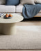 Kansas Floor Rug in Oyster/Natural, under a round cream coffee table in front of a grey sofa