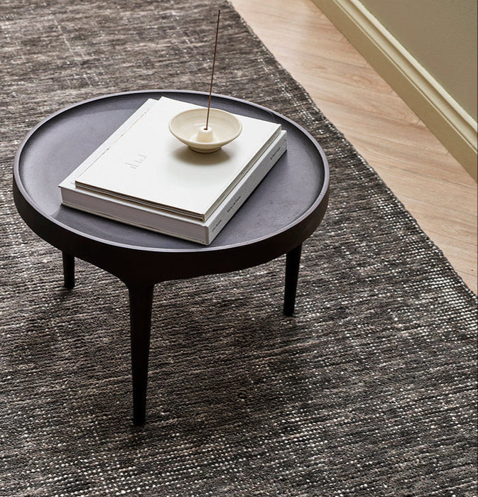 Corbett Floor Rug in Peat, close up under a round black side table with books and incense