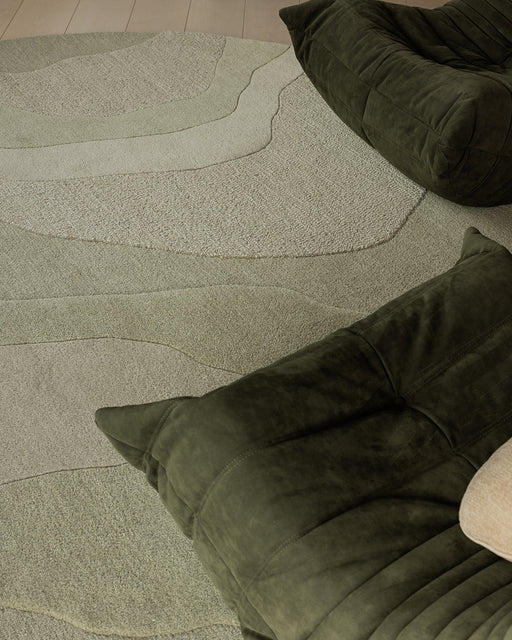 Edgewater Round Floor Rug in Pistachio, close up with dark green lounge chairs, showing the carved wave pattern