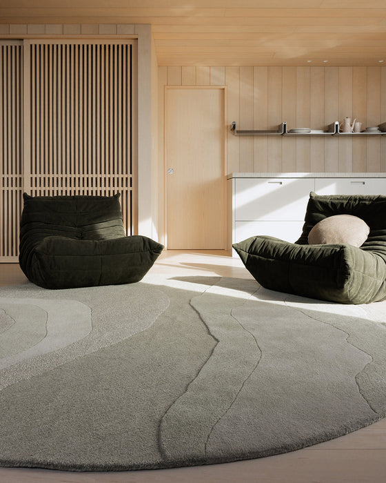 Edgewater Round Floor Rug in Pistachio, under dark green lounge chairs in a timber lined living room