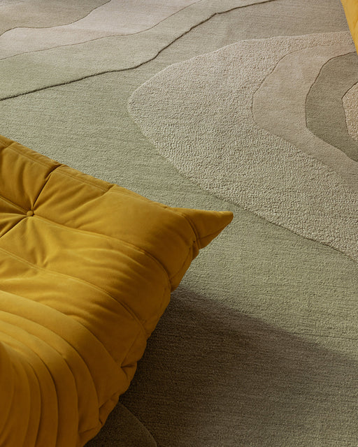 Edgewater Floor Rug in Pistachio, close up beside a mustard lounge chair, showing the carved wave pattern