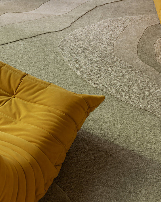 Edgewater Floor Rug in Pistachio, close up beside a mustard lounge chair, showing the carved wave pattern