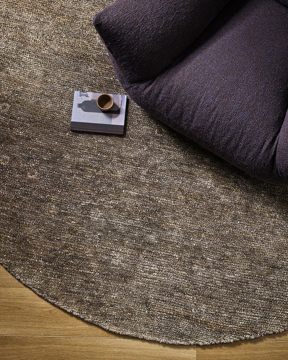Fairbanks Round Floor Rug in Fossil, seen from above beside a dark armchair, showing the pile texture