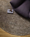 Fairbanks Round Floor Rug in Fossil, seen from above beside a dark armchair, showing the pile texture