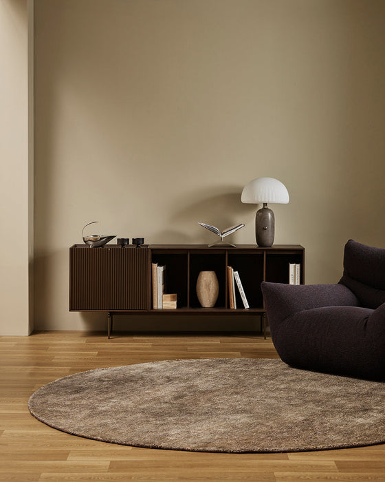 Fairbanks Round Floor Rug in Fossil, in a living room with a timber sideboard and dark armchair