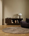 Fairbanks Round Floor Rug in Fossil, in a living room with a timber sideboard and dark armchair