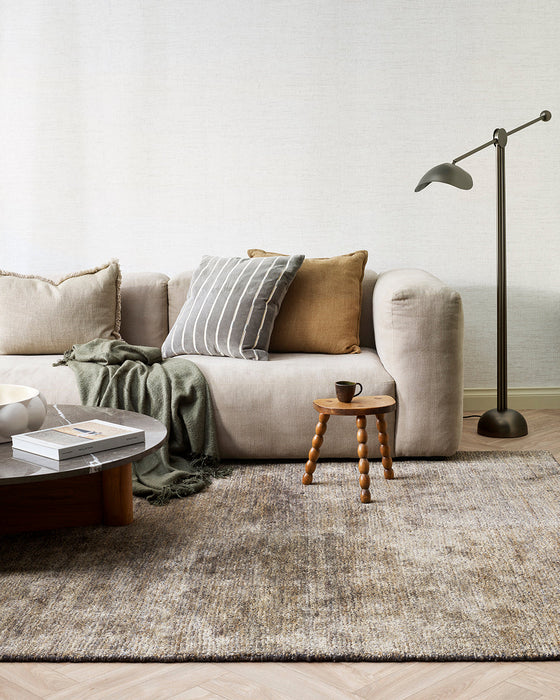 Fairbanks Floor Rug in Fossil, styled in a living room with a cream sofa and floor lamp