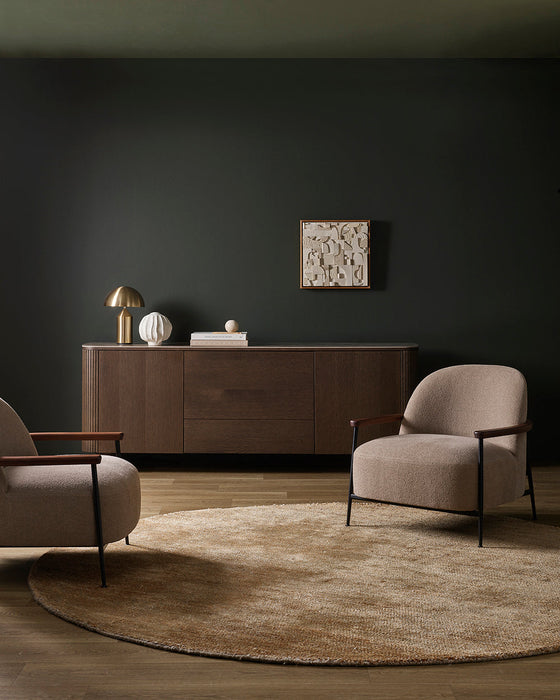 Fairbanks Round Floor Rug in Sand, in a dark green room with a timber sideboard and two armchairs