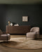 Fairbanks Round Floor Rug in Sand, in a dark green room with a timber sideboard and two armchairs
