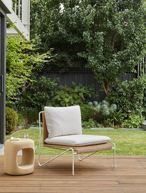 Blossom Armchair on a timber deck in a leafy garden beside a sculptural stone side table