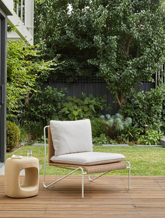 Blossom Armchair on a timber deck in a leafy garden beside a sculptural stone side table