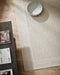 Vermont Floor Rug in Sand, seen from above beside a dark timber table with a ceramic bowl