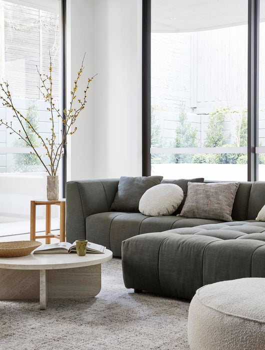 Tepih Dune Rug in Oatmeal, under a dark green modular sofa and a round white coffee table