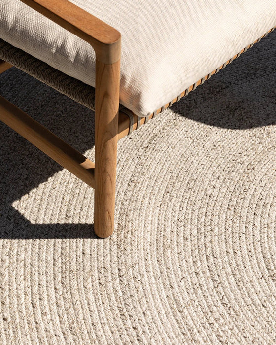Mornington Round Floor Rug in Pale Sand, close up under a timber and cream outdoor chair, showing the braided weave