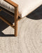 Mornington Round Floor Rug in Pale Sand, close up under a timber and cream outdoor chair, showing the braided weave