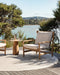 Mornington Round Floor Rug in Pale Sand, on a timber deck with an outdoor armchair and side table above a bay