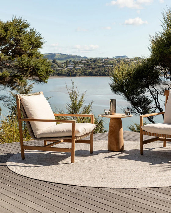 Mornington Round Floor Rug in Pale Sand, on a timber deck overlooking the water with two outdoor armchairs