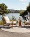 Mornington Round Floor Rug in Pale Sand, on a timber deck overlooking the water with two outdoor armchairs