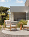 Mornington Round Floor Rug in Pale Sand, on a timber deck beside a white house with two outdoor armchairs