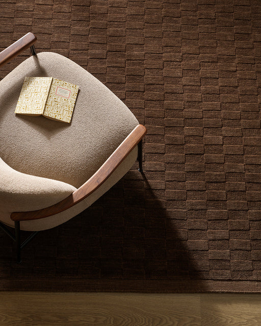 Hugo Floor Rug in Espresso, seen from above with a cream armchair, showing the block weave pattern