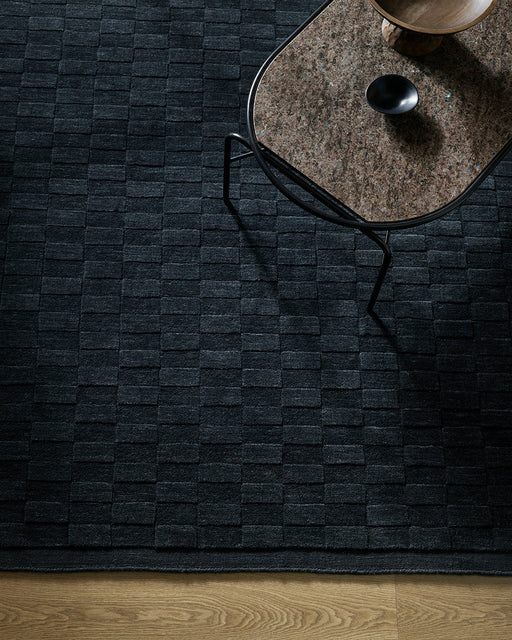 Hugo Floor Rug in Midnight, seen from above with a glass side table, showing the block weave pattern