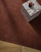 Linden Floor Rug in Brick, seen from above with a marble side table holding red flowers