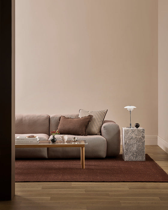 Linden Floor Rug in Brick, in a living room with a low pink sofa, timber coffee table and marble side table
