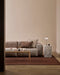Linden Floor Rug in Brick, in a living room with a low pink sofa, timber coffee table and marble side table