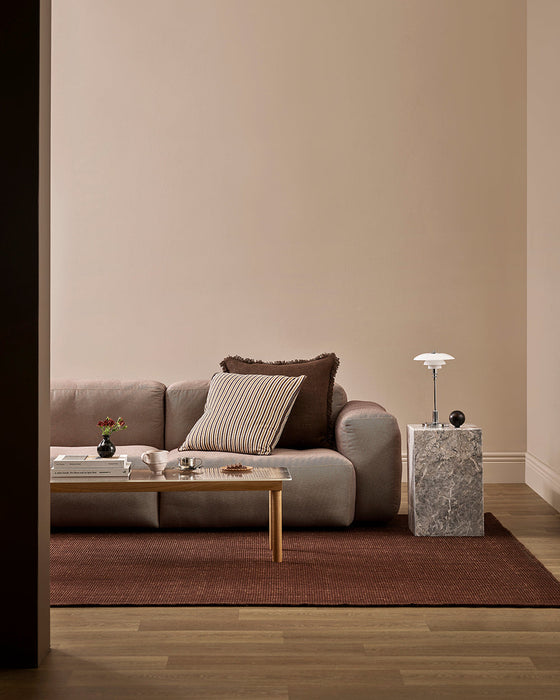 Linden Floor Rug in Brick, in a living room with a pink sofa, striped cushions and timber coffee table
