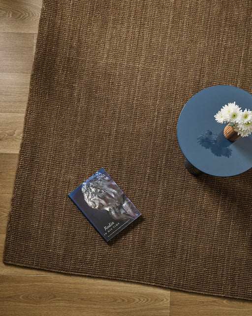 Linden Floor Rug in Ironbark, seen from above with a blue side table and a book, showing the weave